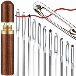 May include: A collection of silver sewing needles in different sizes, with a wooden needle case. A red thread is passed through one needle. The needle case is cylindrical, with a dark brown wooden exterior and a gold-coloured metal band.