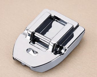 Puede incluir: Un prensatelas de máquina de coser cromado y brillante. Tiene forma rectangular con una parte delantera curvada y una barra en la parte superior. Diseñado para fijarse a una máquina de coser y guiar la tela.