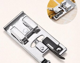 Puede incluir: Un pie de máquina de coser plateado y brillante con un detalle negro. El pie tiene forma rectangular con varios componentes metálicos y una palanca curva. Una pequeña incrustación circular muestra un primer plano del pie.