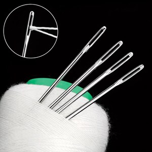May include: A close-up shot of silver sewing needles with white thread, emerging from a white cotton reel. The needles have large eyes for easy threading. The image is set against a black background, highlighting the needles and thread.
