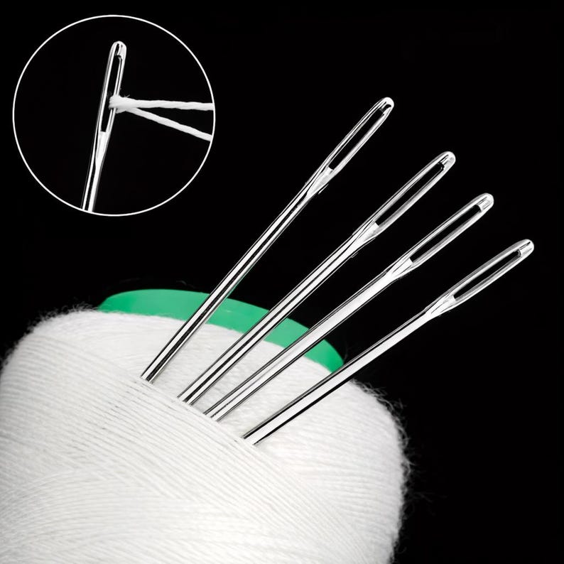 May include: A close-up shot of silver sewing needles with white thread, emerging from a white cotton reel. The needles have large eyes for easy threading. The image is set against a black background, highlighting the needles and thread.