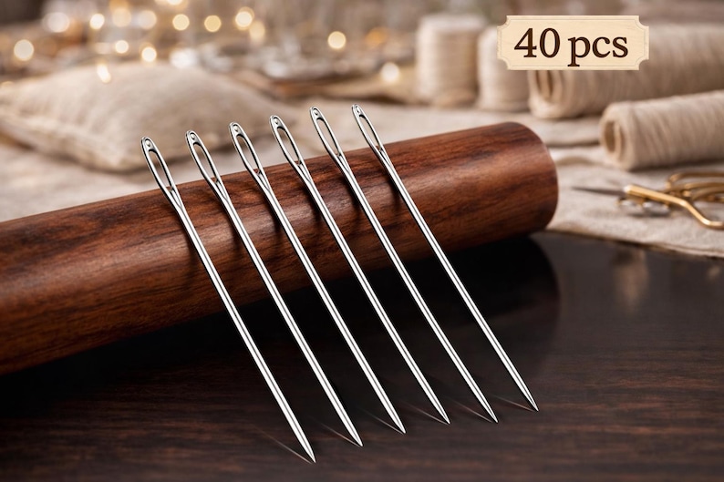 May include: A set of silver sewing needles displayed on a dark wooden spool. The needles are long and thin, with a visible eye. The image includes the text "40 pcs".