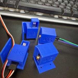 May include: Four blue 3D-printed electronic components, each marked with "JG". The components feature different designs, including a small light, a connector, and a gold-coloured port. Wires of various colours extend from the components.