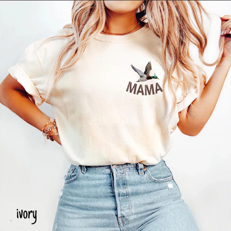 Puede incluir: Camiseta color marfil con un gr&aacute;fico de pato y la palabra "MAMA" impresa. El pato est&aacute; representado en vuelo con detalles en las plumas de las alas. Estilo casual.