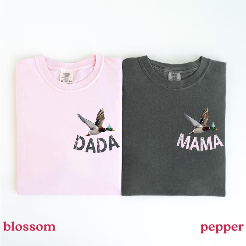 Puede incluir: Dos camisetas, una rosa flor y otra gris pimienta, cada una con un dise&ntilde;o de pato volador. La camiseta rosa tiene la palabra "DADA" y la camiseta gris tiene la palabra "MAMA" impresa debajo.