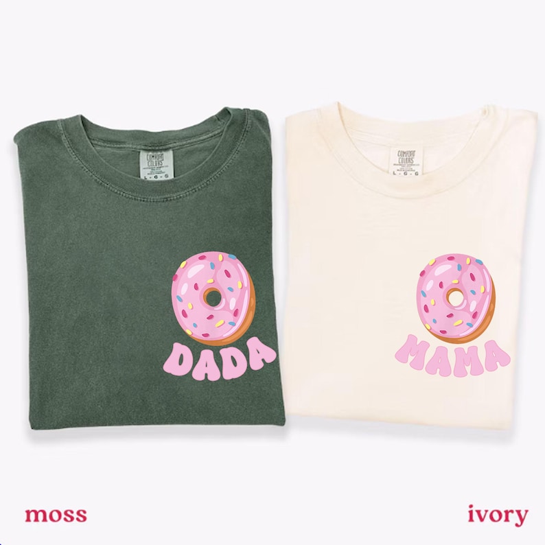 May include: Two t-shirts, one moss green and one ivory, each featuring a pink donut graphic with sprinkles. The moss green shirt has the word "DADA" below the donut, while the ivory shirt says "MAMA".