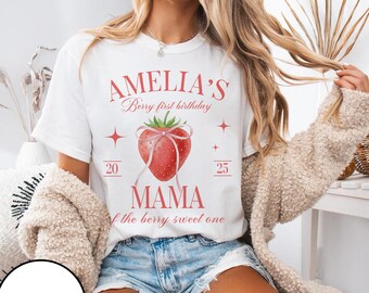 May include: White t-shirt with a strawberry graphic and the text "AMELIA'S Berry first birthday" in red. The design includes a strawberry with a bow, the word "MAMA", and the phrase "the berry sweet one".