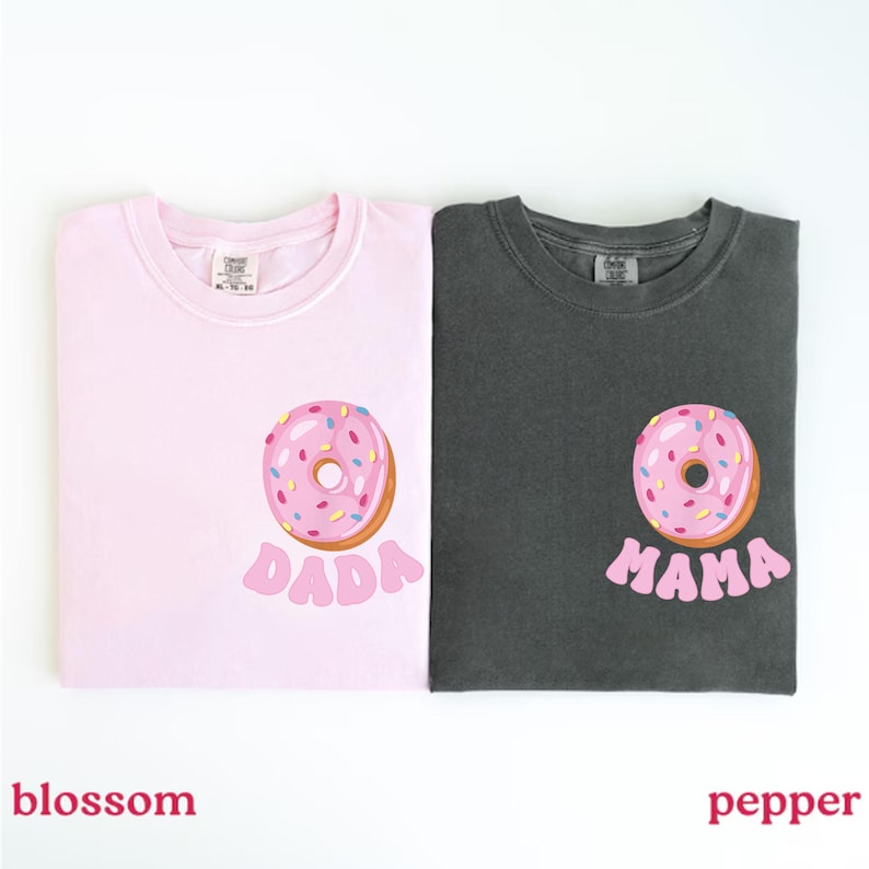 May include: Two t-shirts, one blossom pink and one pepper gray, each featuring a donut graphic. The pink shirt has the word "DADA" below the donut, while the gray shirt says "MAMA". The donuts have pink frosting and colorful sprinkles.