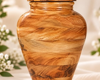 May include: A wooden cremation urn with a smooth, polished finish, featuring a distinct natural grain pattern in shades of light and dark brown. The vessel has a rounded body, a tapered base, and a matching circular lid that sits securely on top.
