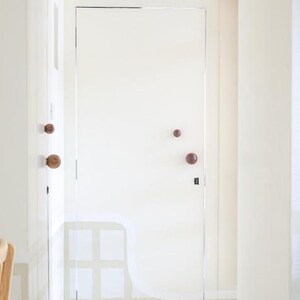May include: A bright white door with two wooden knobs and a dark lock. The door is in a white hallway with a painting on the left and a window on the right. The door is closed.
