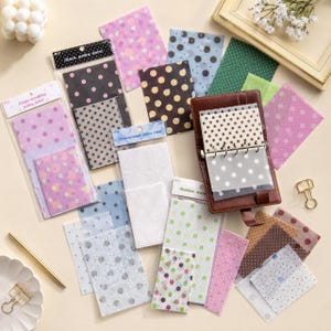 Può includere: Una collezione di fogli di carta velina traslucida con vari motivi a pois in colori tra cui rosa, nero, bianco, verde e marrone. Alcuni fogli sono confezionati in buste di plastica trasparente con etichette, mentre altri sono sciolti o in un raccoglitore in pelle.