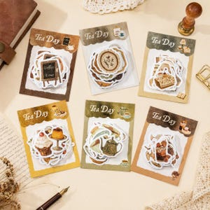 Puede incluir: Seis tarjetas de papel rectangulares etiquetadas como Tea Day, cada una con una pila de pegatinas troqueladas. Las pegatinas presentan ilustraciones estilo acuarela de teteras, tazas, postres y letreros de café en tonos marrones y crema.