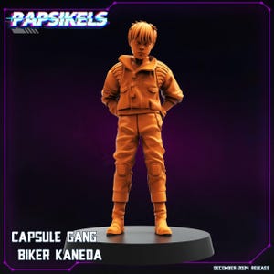 Op de afbeelding: Oranje plastic figuur van een jong persoon die een jas en broek draagt. Het figuur staat op een zwarte basis. De tekst "CAPSULE GANG BIKER KANEDA" is onder de basis afgedrukt.