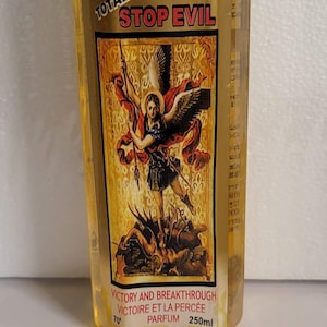 Puede incluir: Una botella hexagonal transparente de perfume "TOTAL STOP EVIL" con una etiqueta dorada que presenta una ilustración de una figura con alas. La botella contiene 250 ml de perfume y tiene una tapa blanca con la inscripción "TOTAL STOP EVIL".