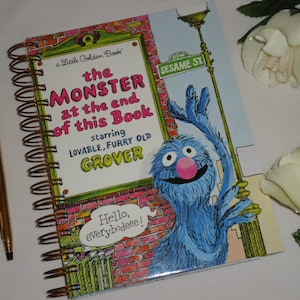 May include: A spiral-bound notebook featuring the cover of the Little Golden Book titled The Monster at the End of This Book, starring lovable, furry old Grover. The cover shows a blue monster, a brick wall, and the text Hello, everybodeee!