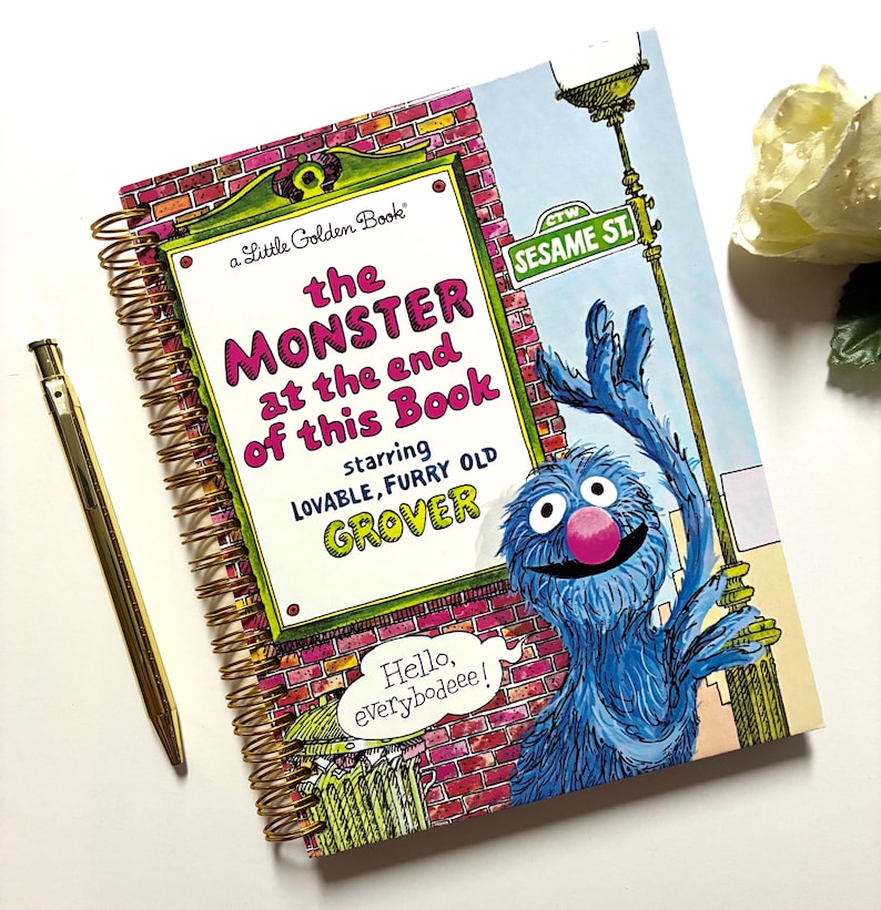 May include: A spiral-bound book titled The Monster at the End of This Book starring lovable, furry old Grover, featuring a blue monster character, a brick wall background, and a speech bubble saying Hello, everybodeee! next to a gold pen.