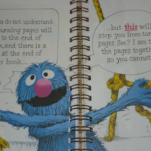 May include: A spiral-bound children's book page featuring a blue furry monster with a pink nose. The monster is holding yellow ropes to tie pages together. Text bubbles read: Maybe you do not understand. You see, turning pages will bring us to the end of this book, and there is a Monster at the end of this book... but this will stop you from turning pages. See? I am tying the pages together so you cannot....
