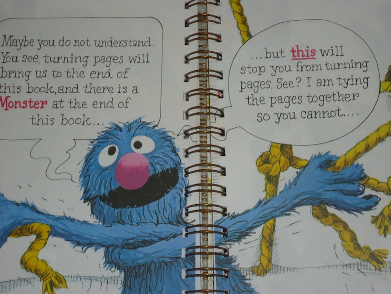 May include: A spiral-bound children's book page featuring a blue furry monster with a pink nose. The monster is holding yellow ropes to tie pages together. Text bubbles read: Maybe you do not understand. You see, turning pages will bring us to the end of this book, and there is a Monster at the end of this book... but this will stop you from turning pages. See? I am tying the pages together so you cannot....