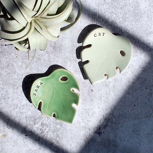 May include: Two green ceramic monstera leaf shaped dishes. One dish says "SARRA" and the other says "C & Y".