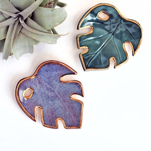 May include: Two ceramic monstera leaf dishes with gold trim. The leaves are a teal green and a purple.
