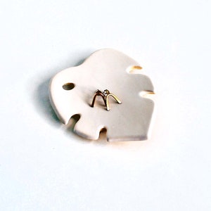 May include: A white ceramic leaf-shaped dish with two gold arch-shaped earrings on top.