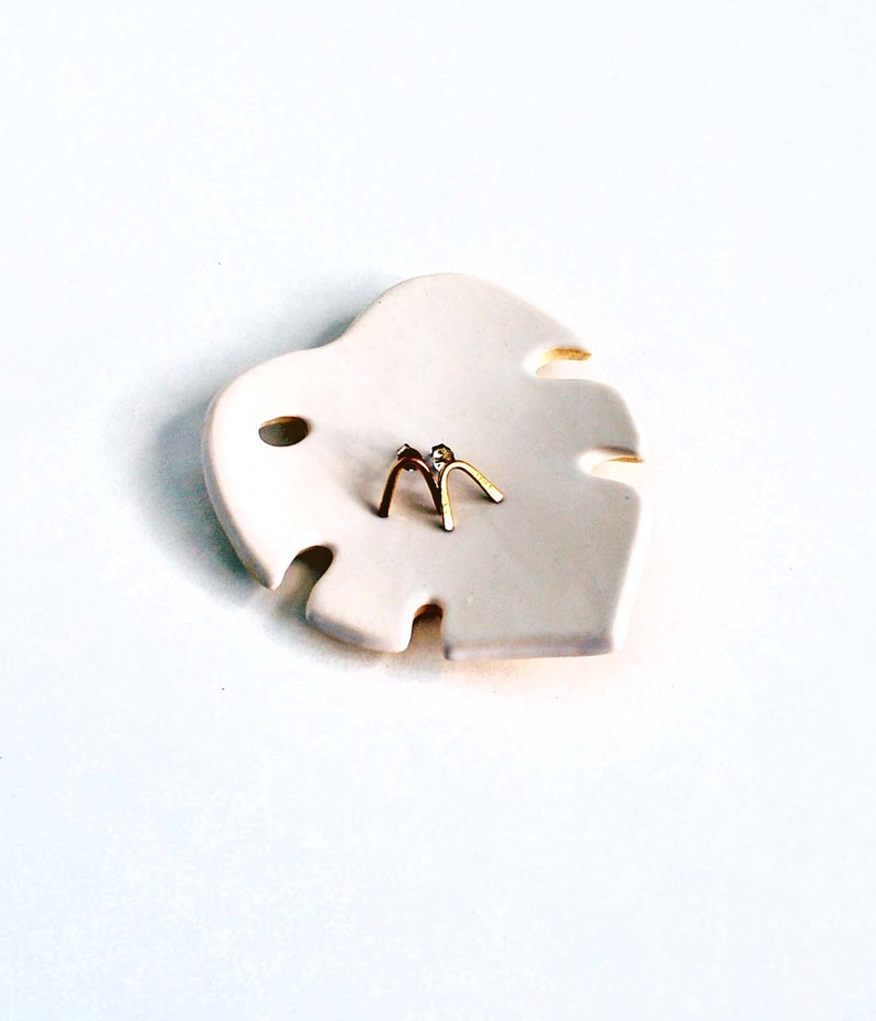 May include: A white ceramic leaf-shaped dish with two gold arch-shaped earrings on top.