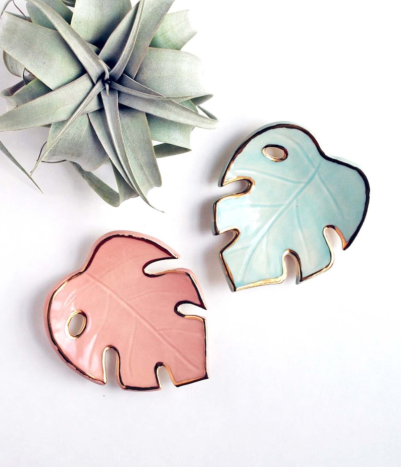 May include: Two ceramic monstera leaf dishes with gold trim. One dish is light blue and the other is pink.