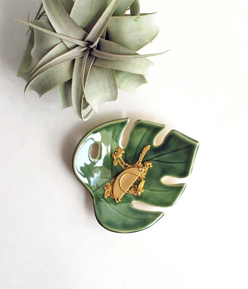 Green Monstera leaf shaped ceramic bowl, used as a jewelry dish to hold necklace and rings.