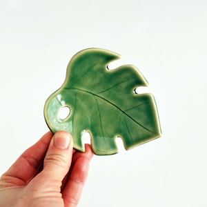 May include: A green ceramic dish shaped like a monstera leaf. The dish has a glossy finish and is perfect for serving snacks or holding jewelry.