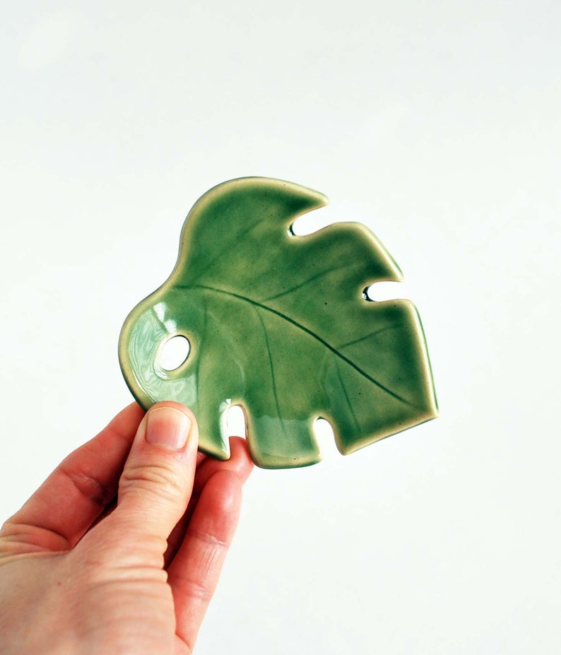 May include: A green ceramic dish shaped like a monstera leaf. The dish has a glossy finish and is perfect for serving snacks or holding jewelry.
