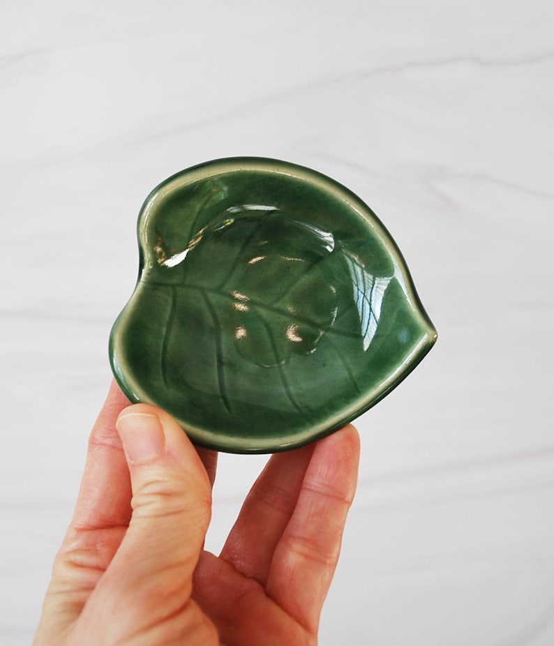 Puede incluir: Un peque&ntilde;o plato de cer&aacute;mica verde con forma de hoja. El plato tiene un acabado brillante y un dise&ntilde;o de hoja en relieve.