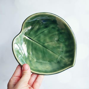May include: A green ceramic dish shaped like a leaf. The dish has a glossy finish and a raised leaf design.