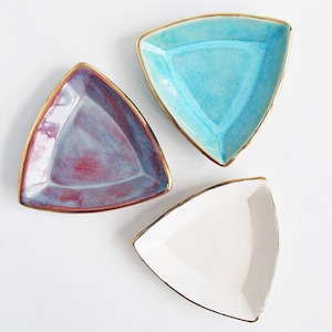 May include: Three triangular ceramic dishes with gold rims. The dishes are in shades of blue, purple, and white.