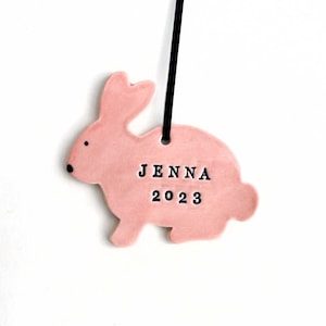 May include: Pink ceramic bunny ornament with the name Jenna and the year 2023.