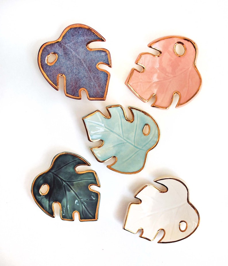 May include: Five ceramic monstera leaf dishes with gold rims. The dishes are in various colors, including purple, pink, blue, green, and white.