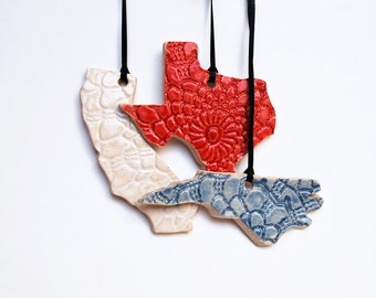 Può includere: Ornamenti in ceramica a forma di stati della California, Texas e Carolina del Nord. L'ornamento del Texas è rosso, quello della California è bianco sporco e quello della Carolina del Nord è blu. Ognuno ha una superficie strutturata e un nastro nero per appenderlo.