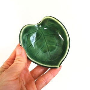Puede incluir: Un peque&ntilde;o plato de cer&aacute;mica verde con forma de hoja. El plato tiene un acabado brillante y un dise&ntilde;o de hoja en relieve.