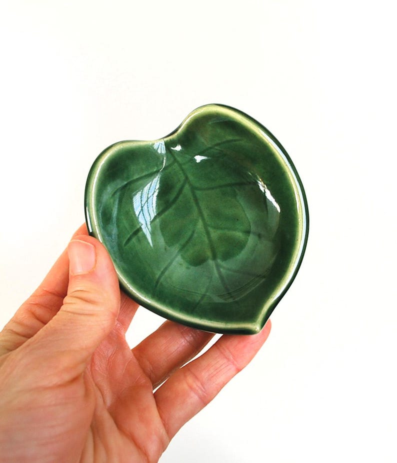 Puede incluir: Un peque&ntilde;o plato de cer&aacute;mica verde con forma de hoja. El plato tiene un acabado brillante y un dise&ntilde;o de hoja en relieve.