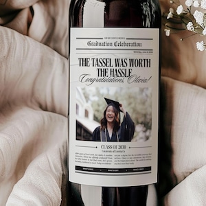 May include: A red wine bottle with a graduation celebration label. The label features a photo of a graduate wearing a cap and gown, and the text "The tassel was worth the hassle. Congratulations Olivia! Class of 2020."