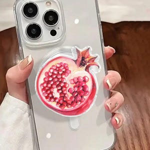 May include: Clear phone case with a vibrant pomegranate design. The case features a detailed illustration of a halved pomegranate, showcasing its red seeds and outer skin. The case is designed to fit a smartphone.