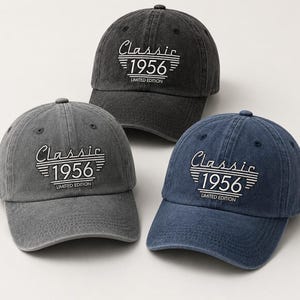 May include: Three baseball caps in shades of gray and blue. Each cap features the text "Classic 1956 Limited Edition" in white script and block letters. The caps have a curved brim and a classic, casual style.
