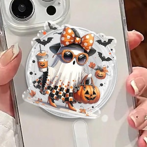 May include: A clear phone case with a Halloween-themed pop socket. The pop socket features a cartoon ghost wearing sunglasses, a bow, and holding a pumpkin. The ghost is surrounded by bats, pumpkins, and a coffee cup. The phone case is clear.