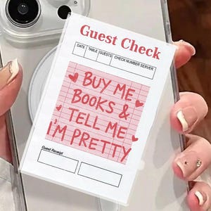 May include: A clear phone case with a white magnetic ring and a printed "Guest Check" design. The check reads "BUY ME BOOKS & TELL ME I'M PRETTY" in pink text with heart accents. The phone case is held by a person.