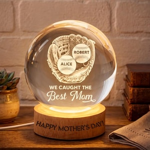 May include: A clear glass sphere with a baseball glove and two baseballs etched inside. The baseballs are labeled "Alice" and "Robert." The base is wood and has the text "Happy Mother's Day!" A unique gift.