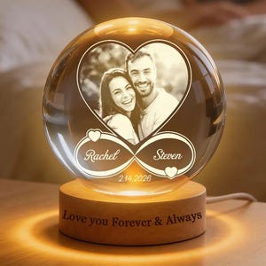 May include: A clear crystal ball with a photo of a couple inside a heart shape. The names "Rachel" and "Steven" are inscribed, along with the date "2.14.2026". The ball sits on a wooden base with the words "Love you Forever & Always".