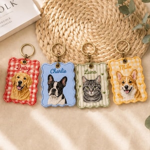 Pode incluir: Quatro porta-chaves retangulares bordados com bordas recortadas e argolas de metal. Cada um apresenta o retrato de um animal de estimação e um nome: um golden retriever chamado Daisy, um bulldog francês Charlie, um gato tigrado Luna e um corgi Milo.