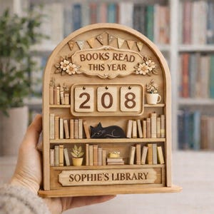 Könnte beinhalten: Holzregal-förmiges Display mit dem Text "BOOKS READ THIS YEAR" und der Zahl "208". Das Display zeigt auch eine schwarze Katze, Miniaturbücher und den Text "SOPHIE'S LIBRARY".