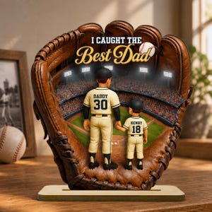 Op de afbeelding: Een honkbal-thema decoratie met een honkbalhandschoen met de tekst "I Caught the Best Dad". Binnenin de handschoen omlijst een honkbalstadion-scène twee figuren in honkbaluniformen. Eén figuur is gelabeld "Daddy 30" en de andere "Henry 18".