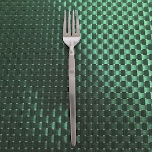 Könnte beinhalten: Eine Edelstahlgabel mit vier Zinken, vor einem strukturierten grünen Hintergrund. Die Gabel hat ein schlichtes, modernes Design, das für den täglichen Gebrauch geeignet ist. Der Griff ist glatt und die Zinken sind gleichmäßig verteilt.