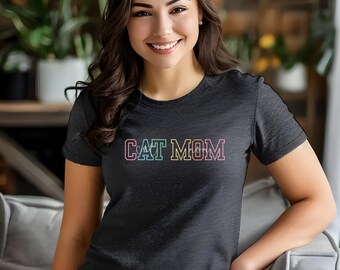 Può includere: Una maglietta nera con la scritta "CAT MOM" in colori arcobaleno.